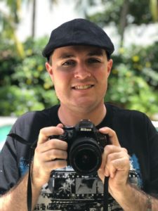 Image of Zack smiling and holding a Nikon camera