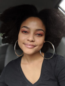 Image of Zahra in a Car Wearing Loop Earrings and Red Eye Shadow 