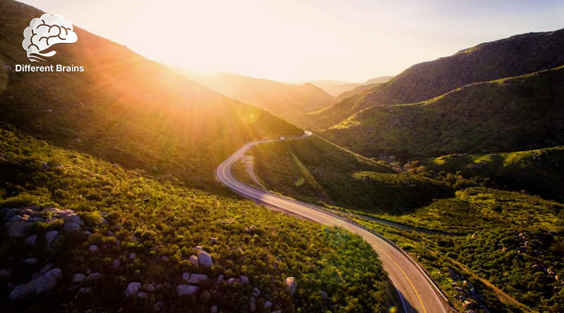 The sun shines over the horizon of a valley, with a road cutting through the middle.
