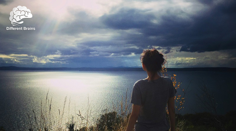 a woman looks at the sea as rays of light appear through clouds