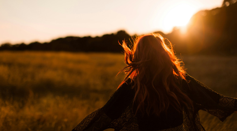 A woman runs through a field with arms outstretched during sunrise