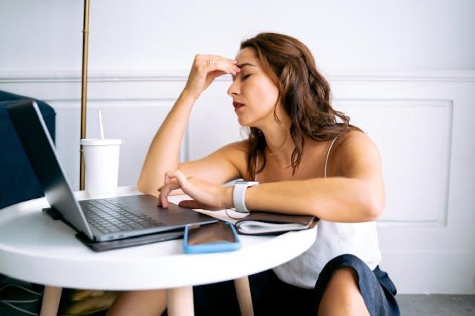 A frustrated woman sitting at her laptop and rubbing her forehead.