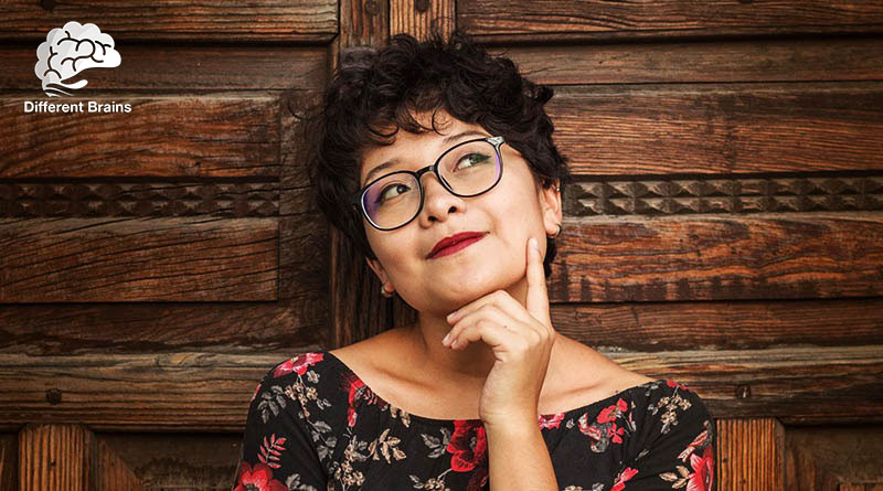 A woman with short hair and glasses gives an inquisitive look with her finger on her chin.