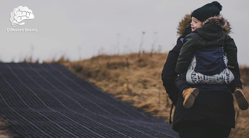 A small child holds on to an adults back as they walk along a track.