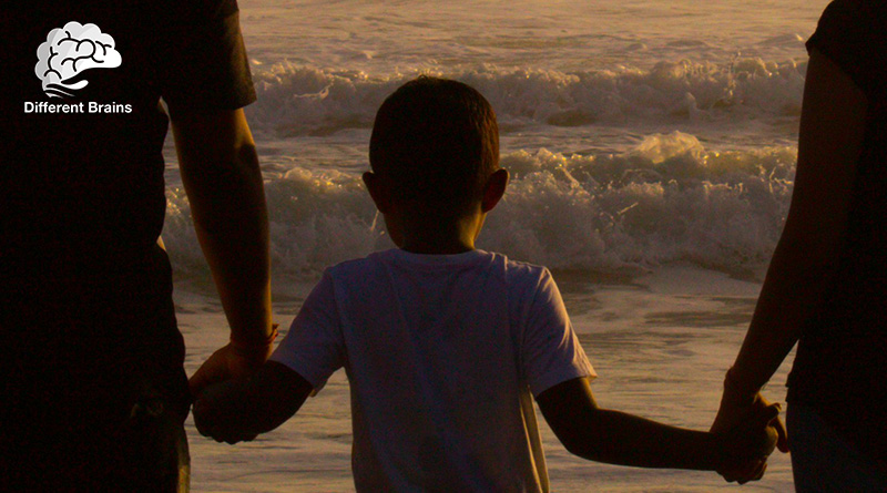 A child has a parent holding each hand as they look at the ocean.