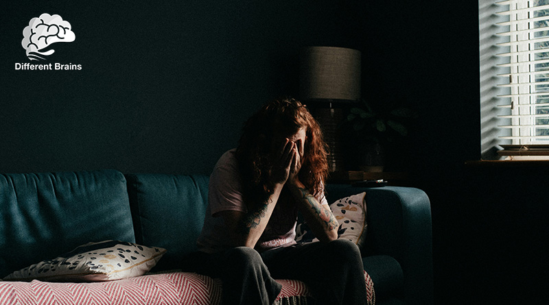 A person sits in a dark room holding their head