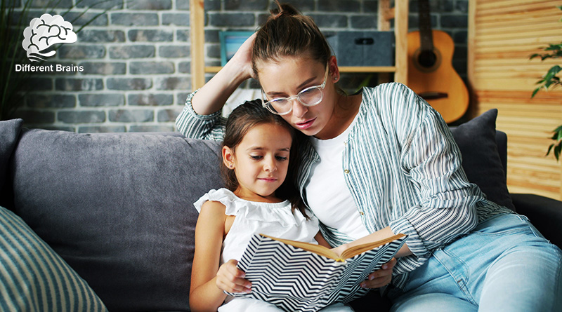 A mother and daughter sit on a couch looking at a book together.