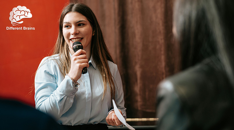 A woman smiles and speaks into a microphone in front of a crowd.