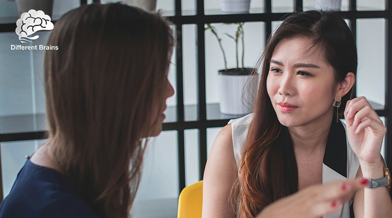 A woman hold her ear while listening to another woman.