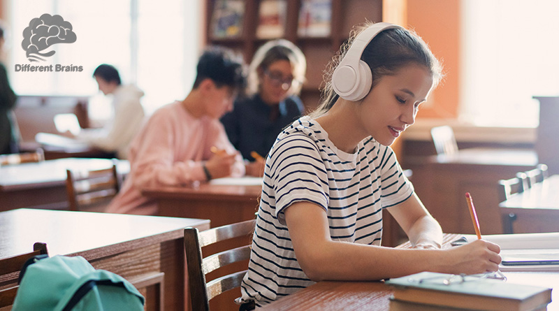 A student sits at a desk writing while wearing headphones